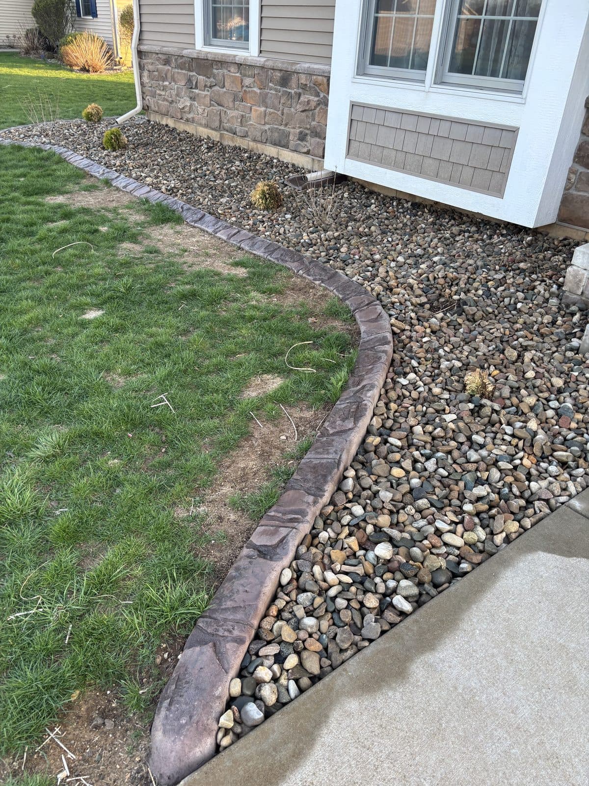 A clean river-rock bed with crisp edging along a home by Fresh Cut Lawns.